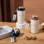 Two white coffee tumblers with brown and black lids on a wooden surface with coffee beans and a book.